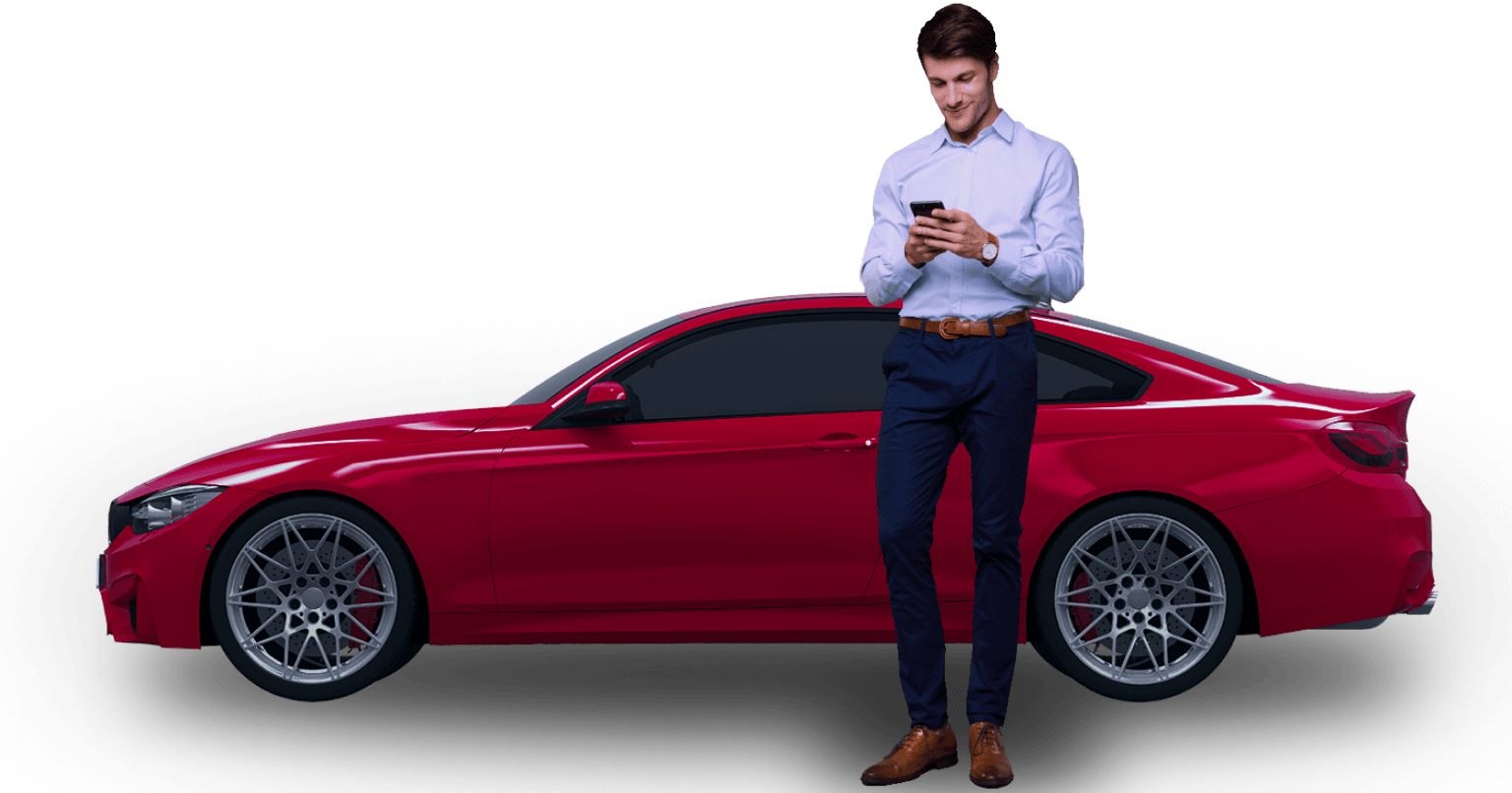 Uśmiechnięty mężczyzna w koszuli i eleganckich spodniach stoi na tle czerwonego BMW coupe. Patrzy na telefon, który trzyma w dłoniach.